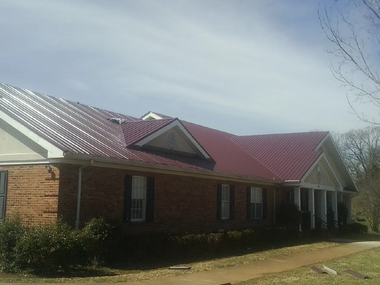 Red metal roof with gabled entries on a long brick building, from a Hail Damage Roof Repair job in Norwich