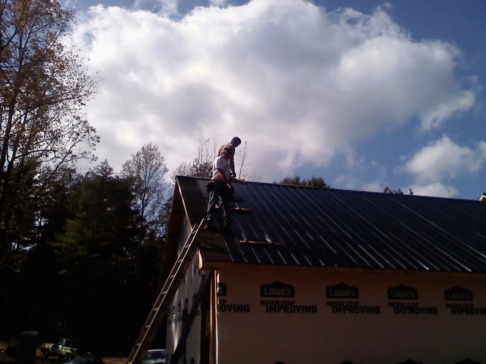 Roofer fastening dark metal panels high against a cloudy sky, from a Roof Inspection job in Norwich