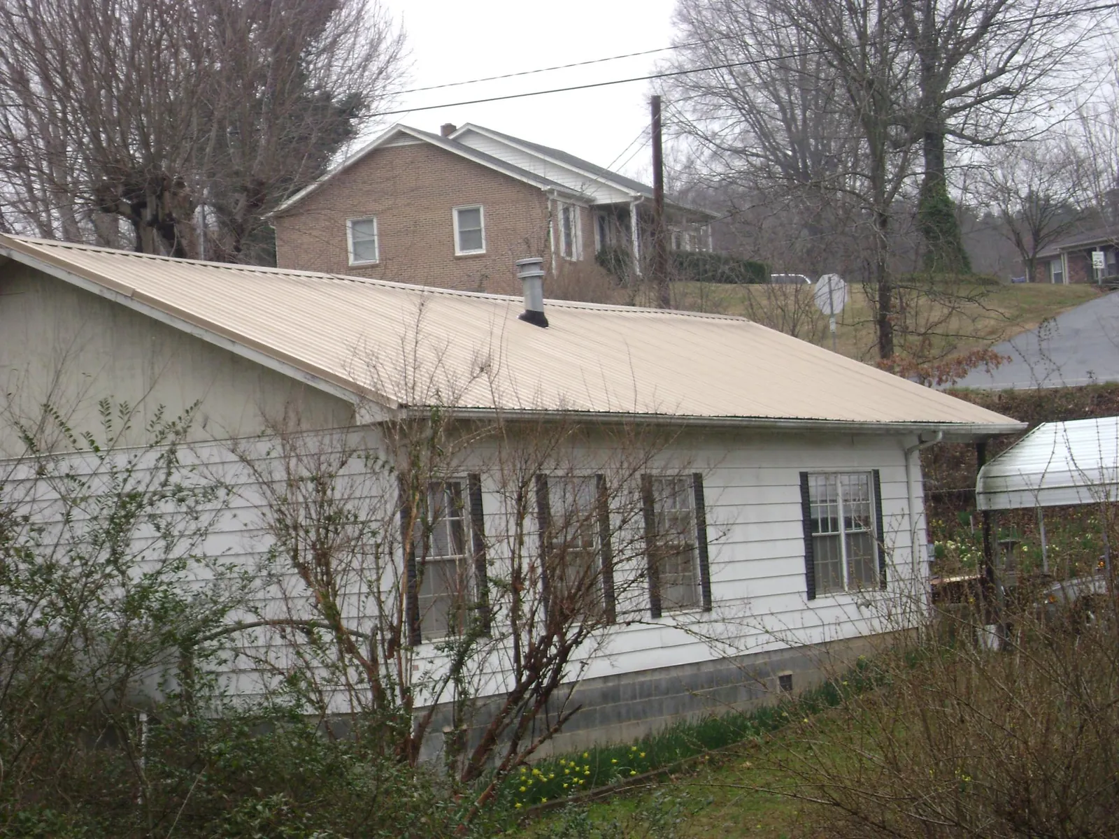 Tan metal roof on a white sided house set into a hillside — Commercial Roofing by Roofing Brothers in Norwich